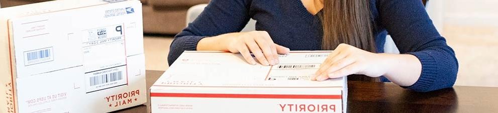 Woman attaching a shipping label to a 优先邮件 box.